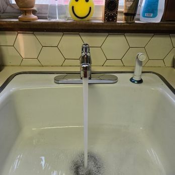 Kitchen sink with water running; white porcelain basin, faucet, and hexagon tile backsplash.