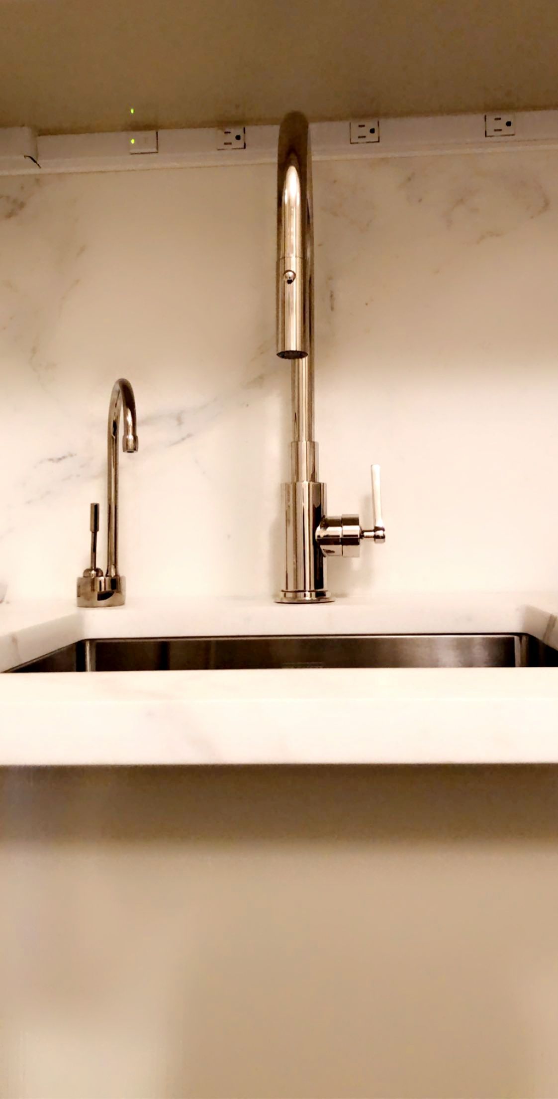 Stainless steel kitchen faucets above a stainless steel sink, set against a white marble countertop.