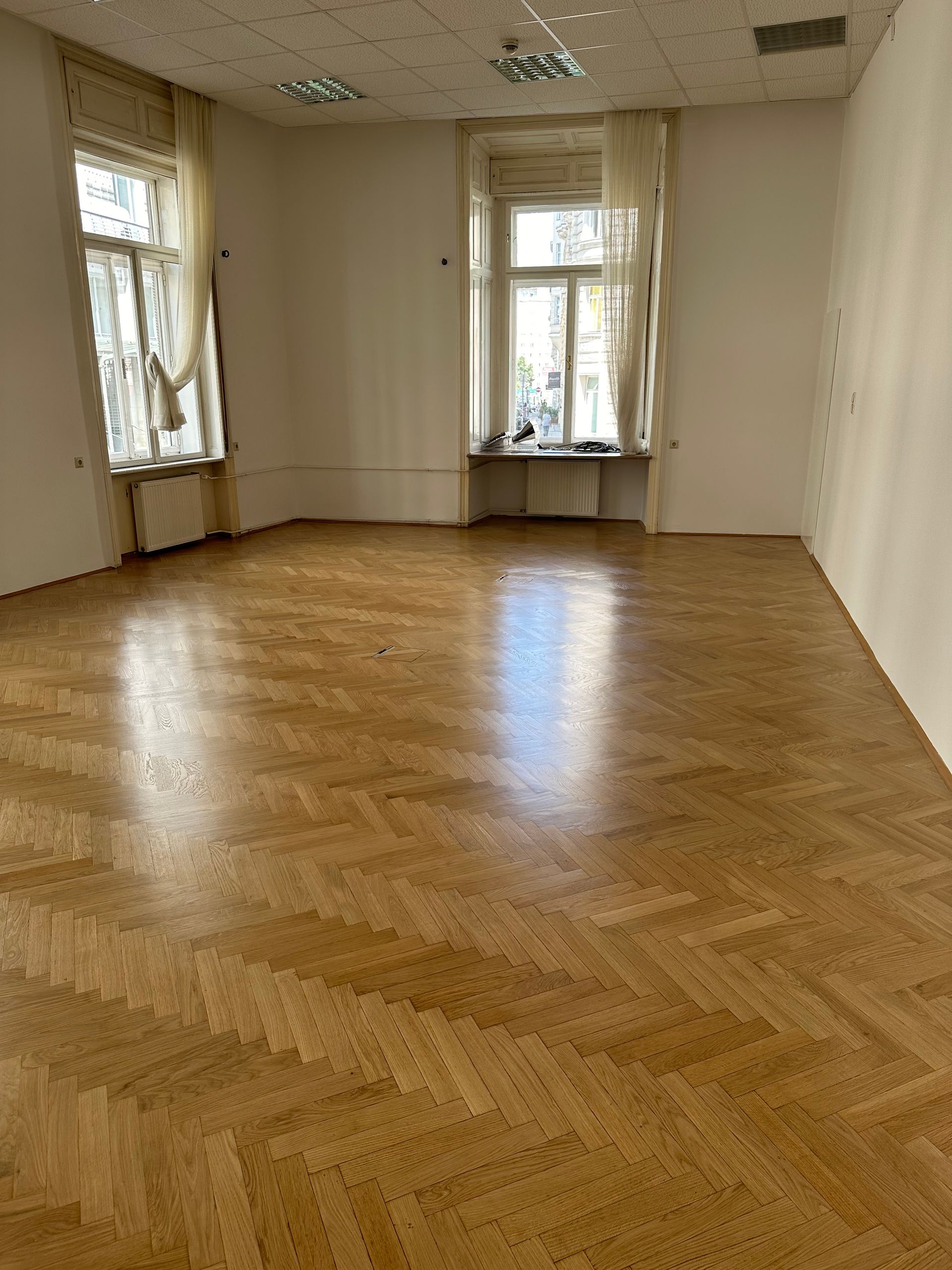 Ein großer leerer Raum mit Holzboden und zwei Fenstern.