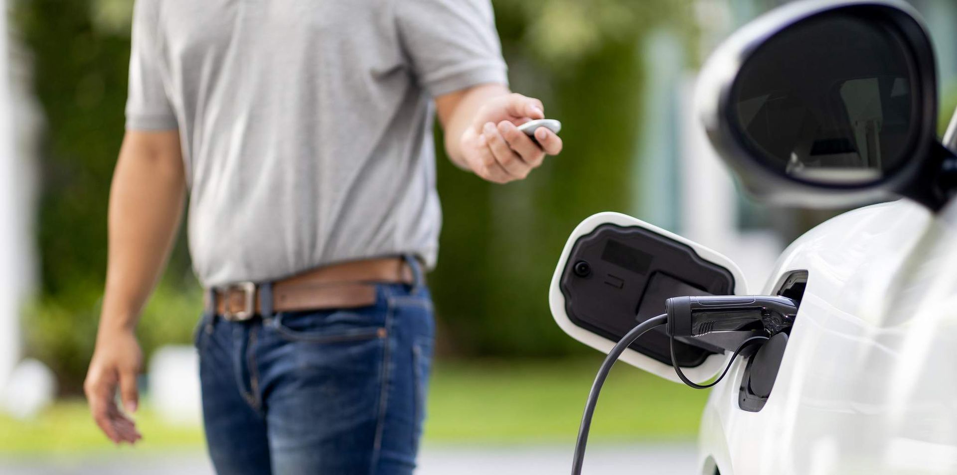 Man met sleutelhanger bij een witte elektrische auto die wordt opgeladen.