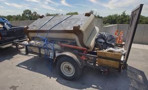 Small trailer loaded with furniture and debris, secured with blue straps outdoors.