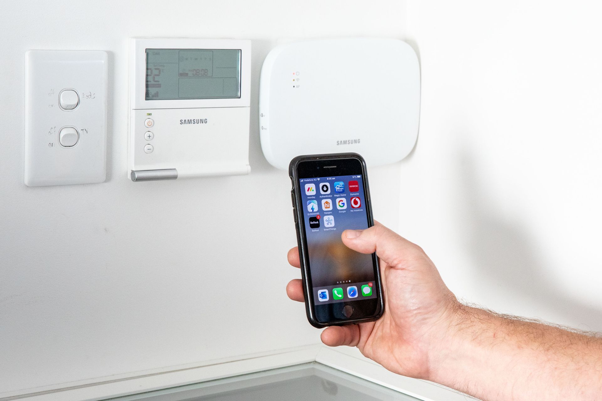A person is holding a cell phone in front of a thermostat.