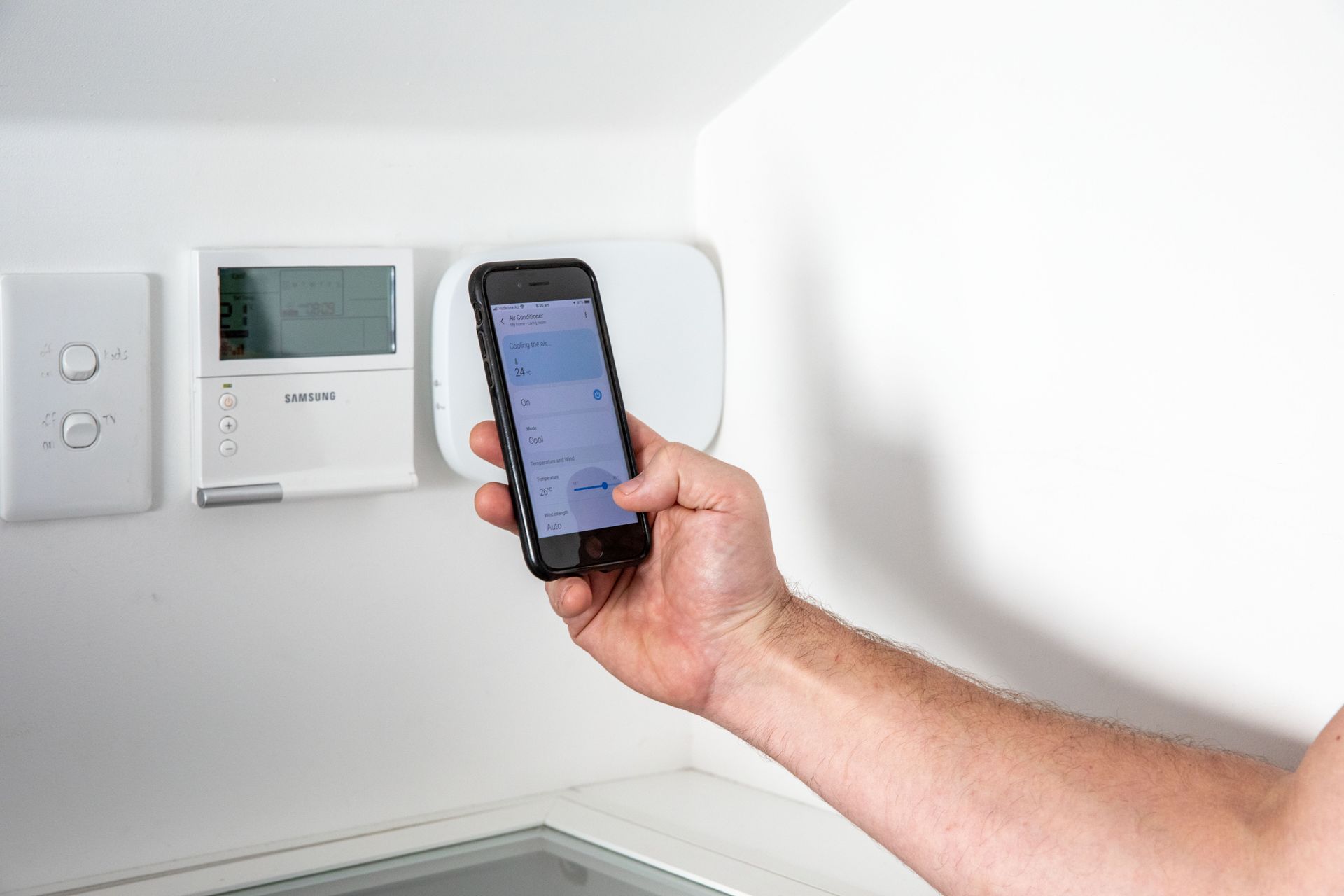 A person is holding a cell phone in front of a thermostat.