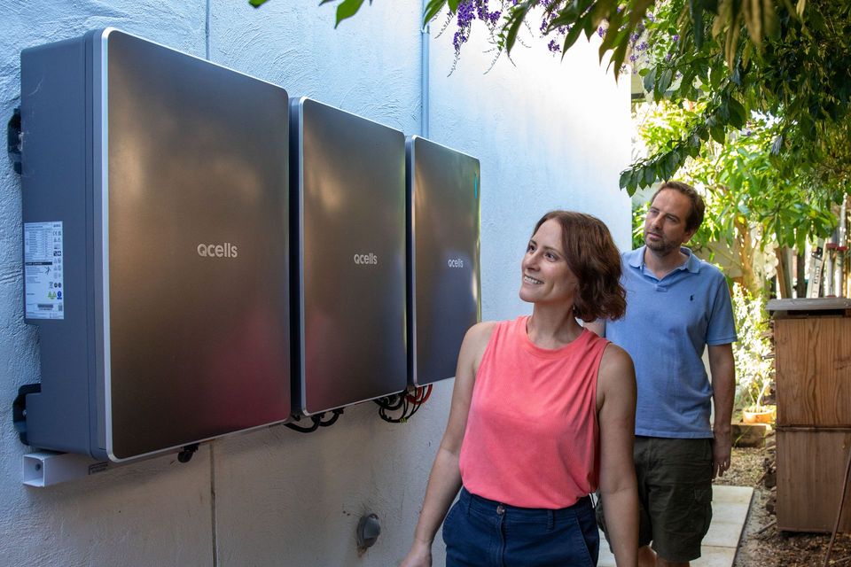 A man and a woman are standing next to a wall with solar panels.