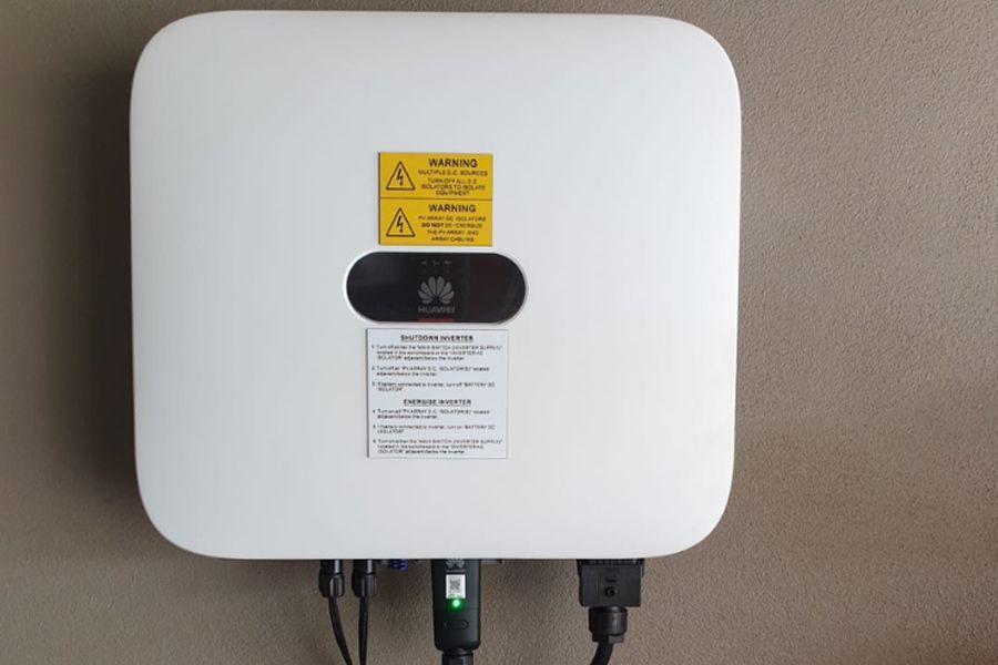 A white solar panel inverter is hanging on a wall.