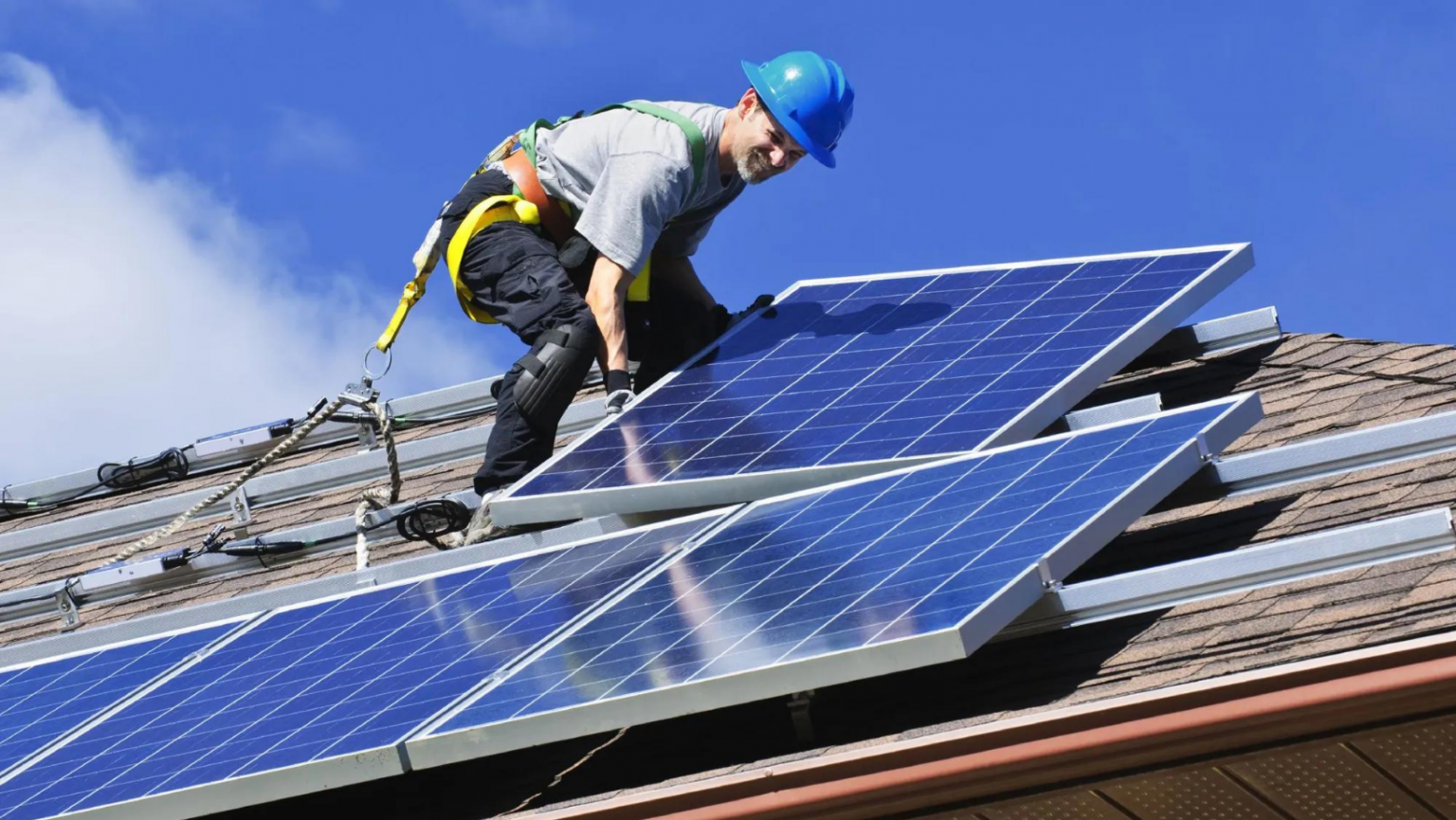 A man is installing solar panels on the roof of a house.