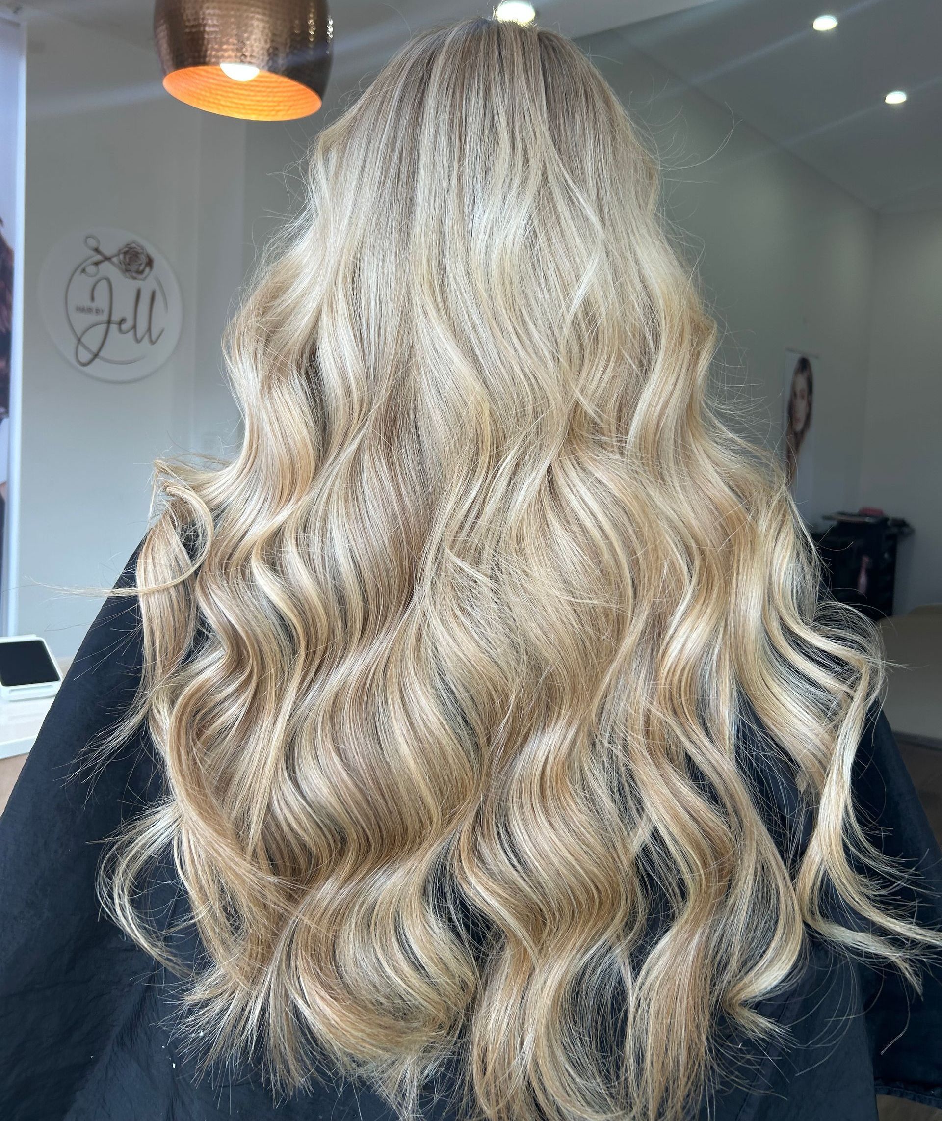 A Woman With Long Blonde Curly Hair is Sitting in a Chair in a Salon — Hair By Jell In Cannonvale, QLD