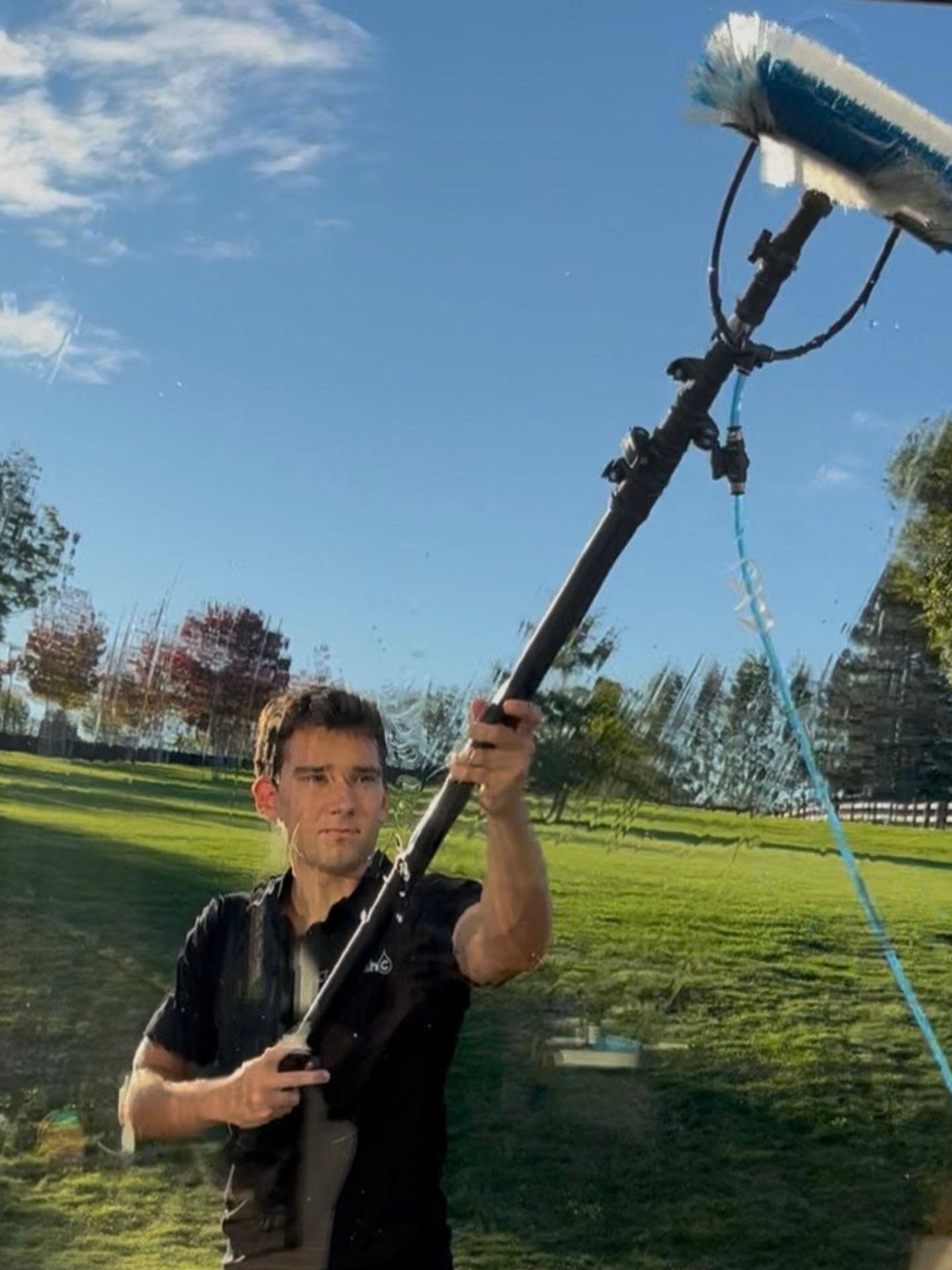 Person using a long pole tool to clean an outside window on a sunny lawn