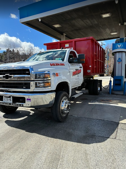 White pickup truck with a red dump trailer at a gas station under a canopy