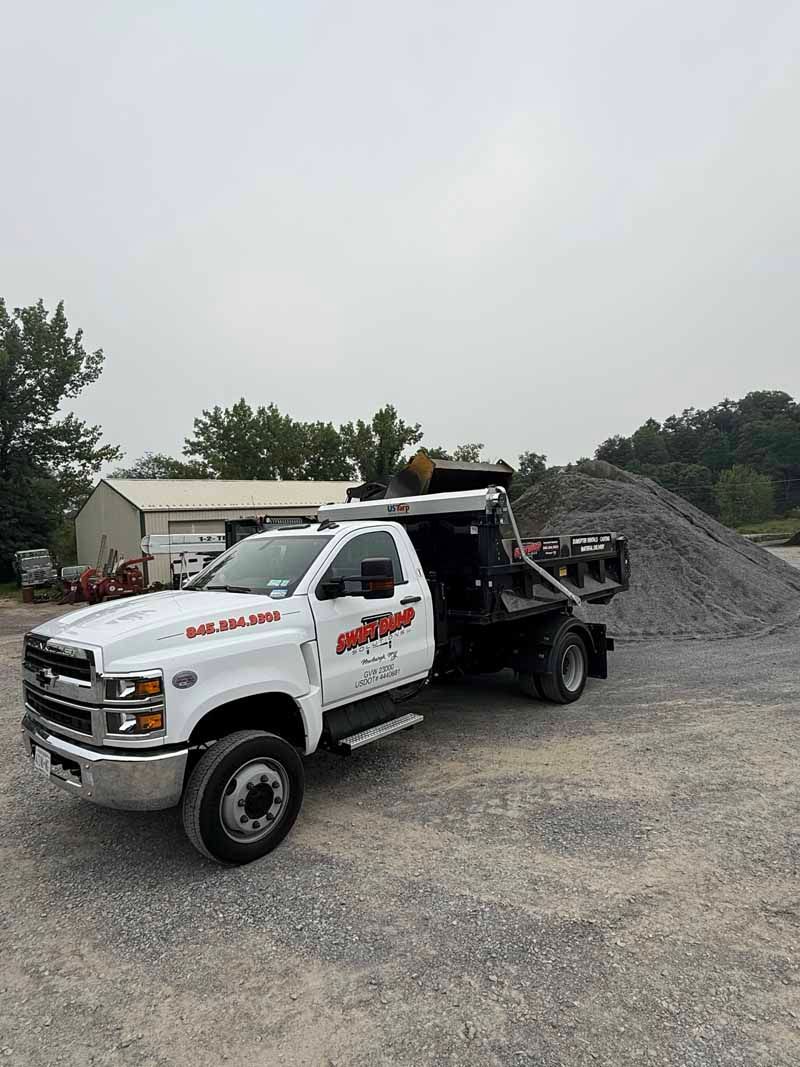 White dump truck with raised bed parked on gravel beside a large pile of rocks at a work site
