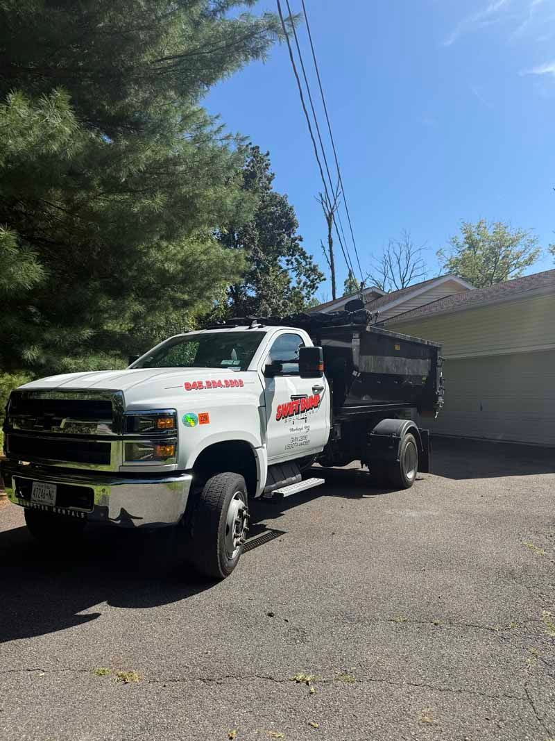 White dump truck parked on gravel beside a garage under a sunny blue sky
