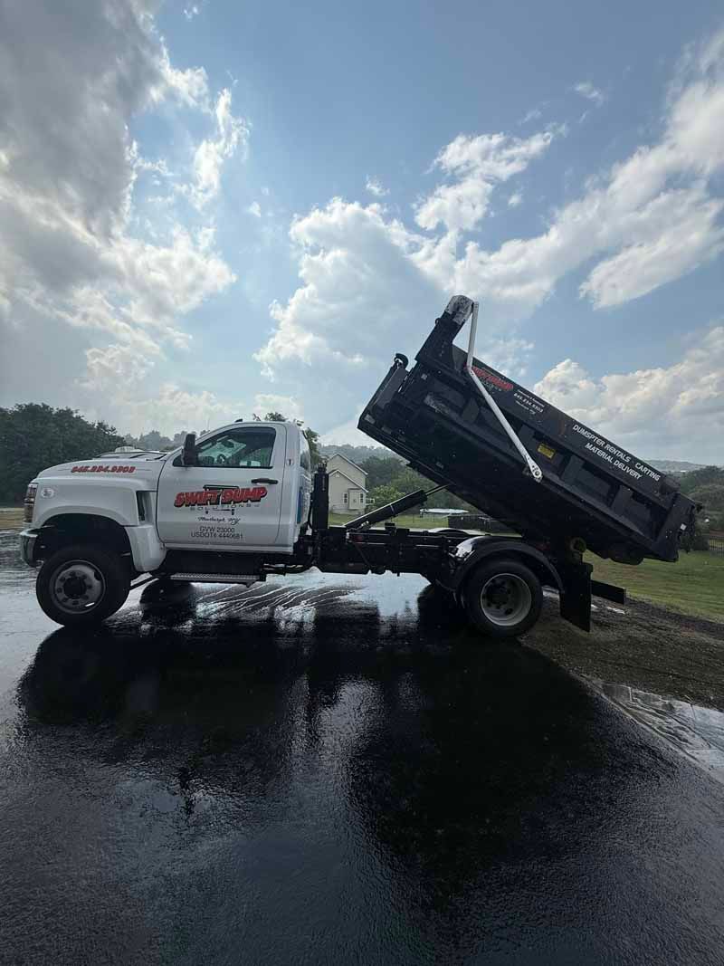 White dump truck with raised bed parked on a wet road under a cloudy sky.