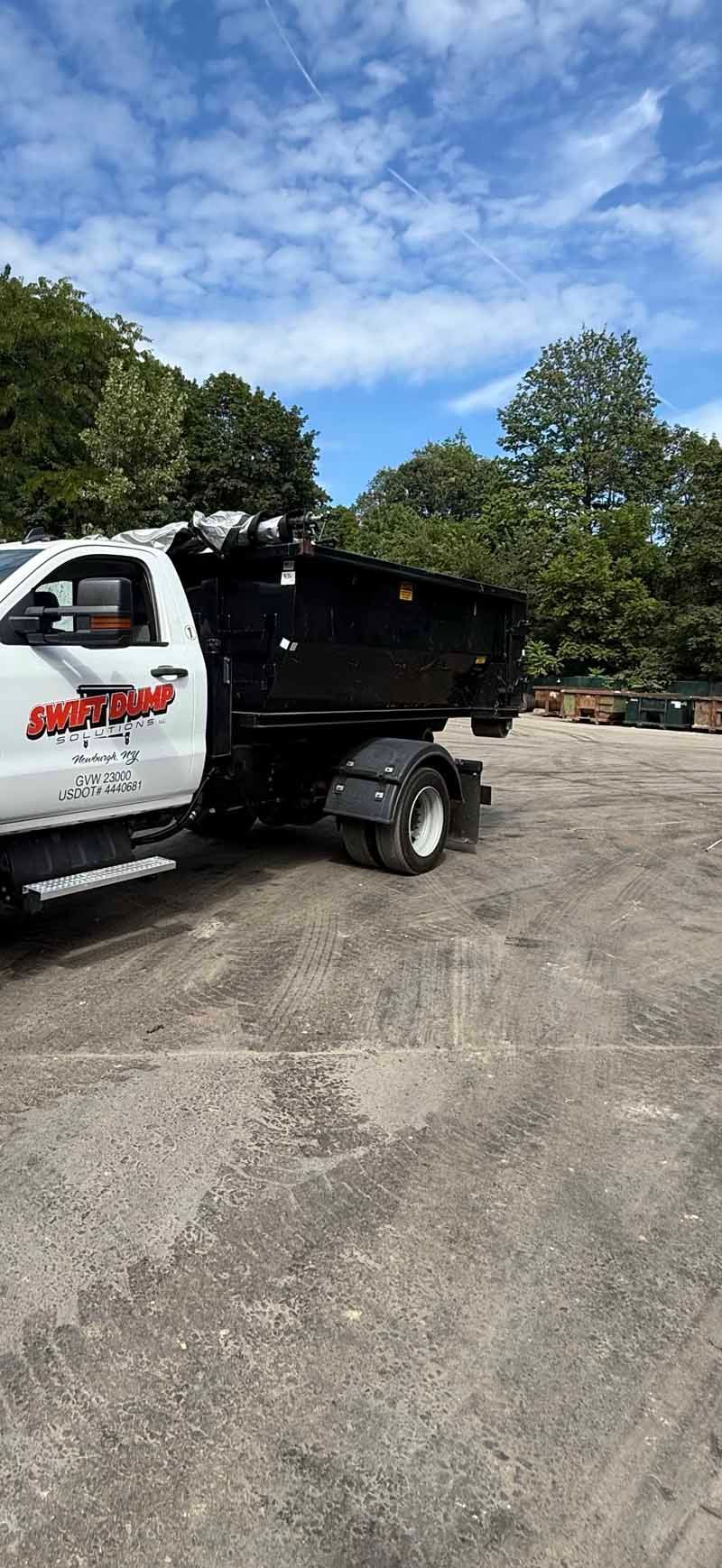 White dump truck parked on a gravel lot under a blue sky with trees nearby
