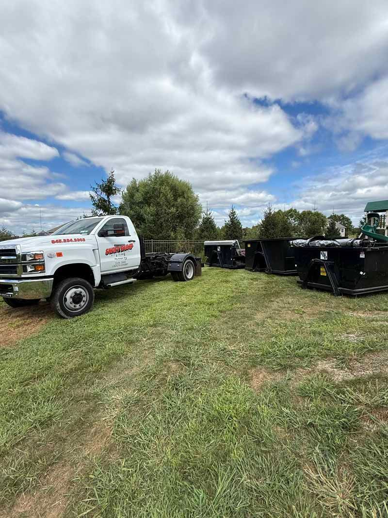 White pickup truck beside a row of black trucks in a grassy lot under a cloudy sky