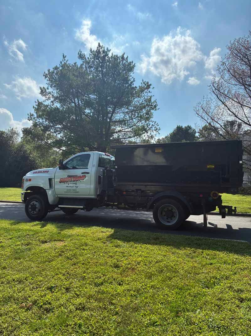 White dump truck parked on grass under a sunny sky with trees in the background
