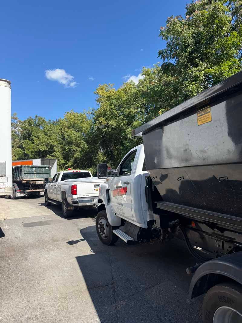 Traffic jam with a white pickup and black dump truck on a sunny street near trees