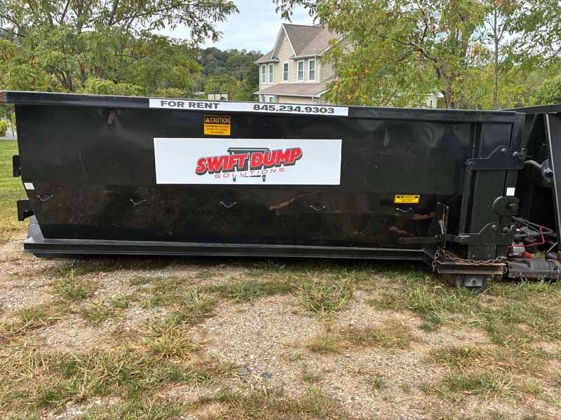 Black SWAT STUMP trailer parked on gravel with trees and houses in the background