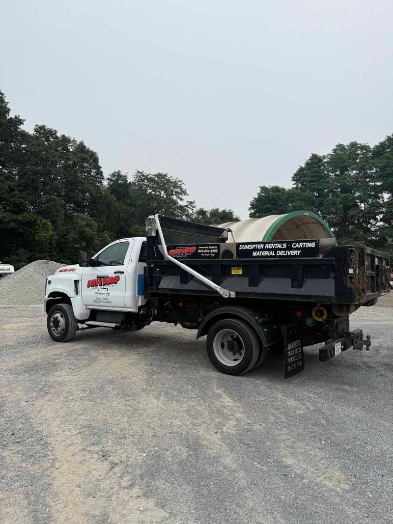 White and black dump truck parked on a gravel lot with trees in the background