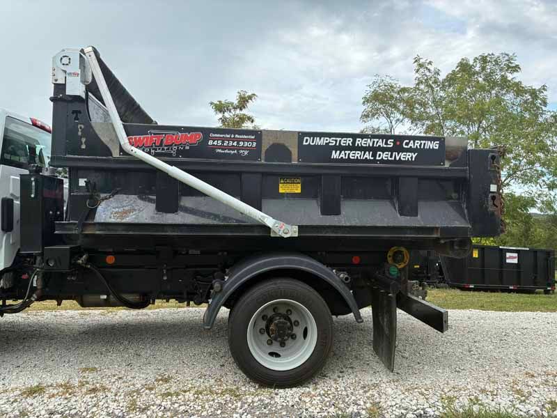 Black dump trailer truck with white crane arm parked on gravel under cloudy sky
