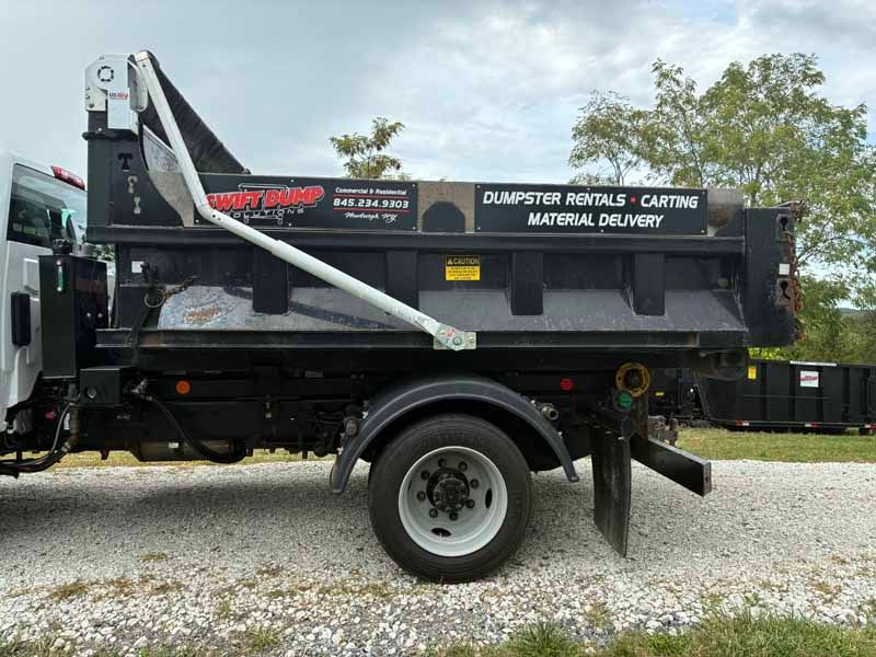 Black dump trailer parked on gravel, labeled “Dumpster Rentals - Carting” under a cloudy sky