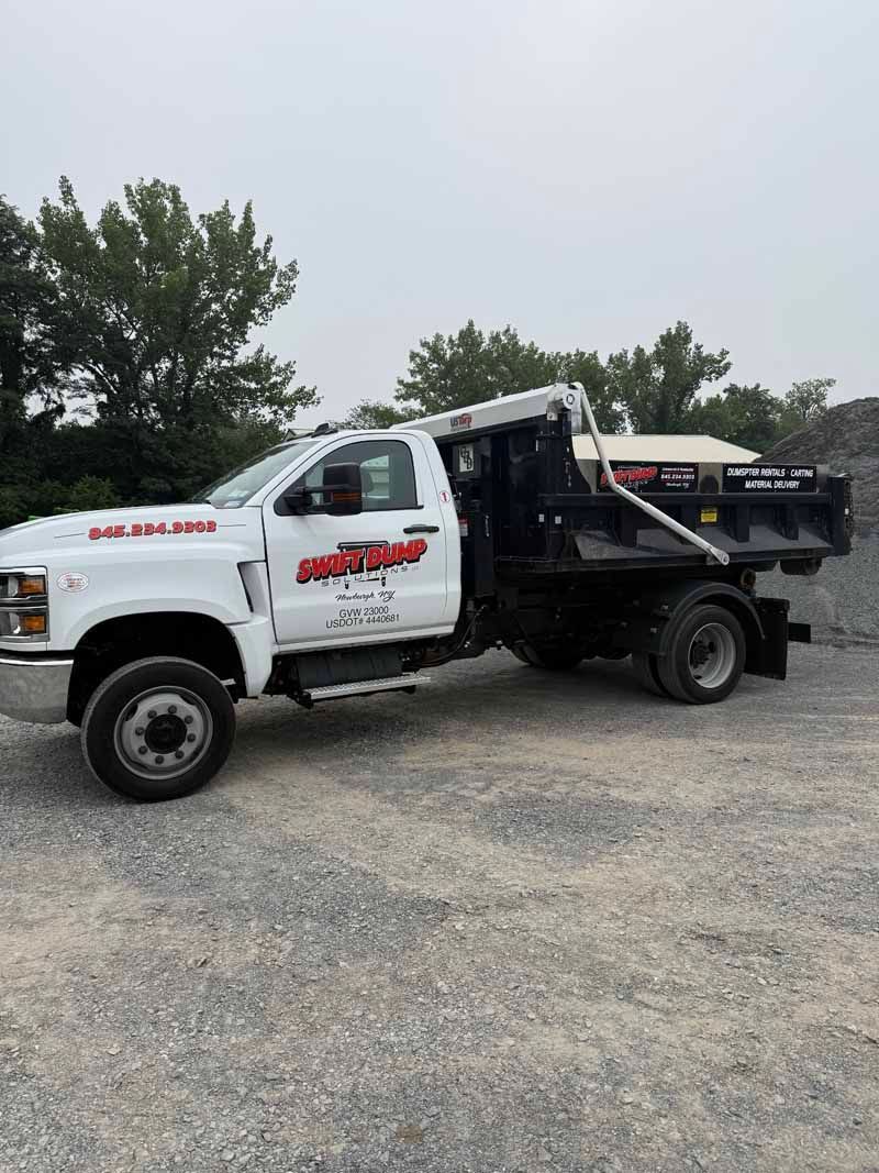 White dump truck with black bed parked on gravel under a cloudy sky.