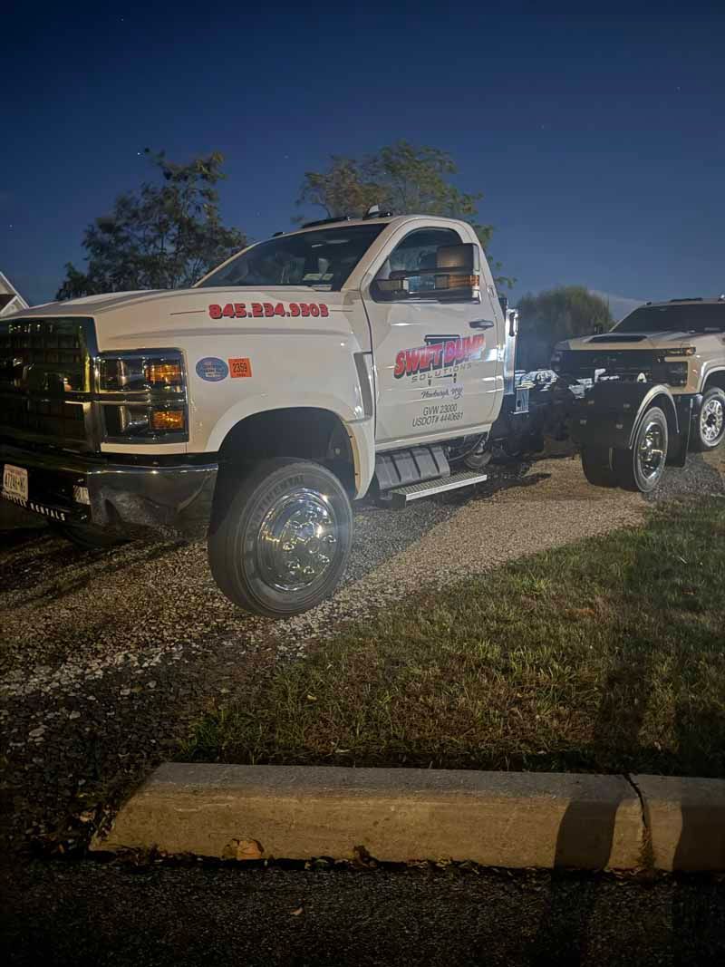 White tow truck parked on gravel at night beside a curb and grass under a dark sky
