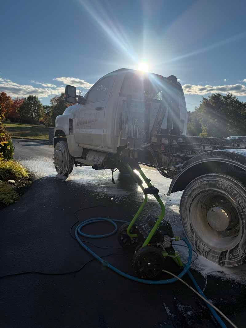 White truck being washed outdoors with bright sun glare and hoses on the ground
