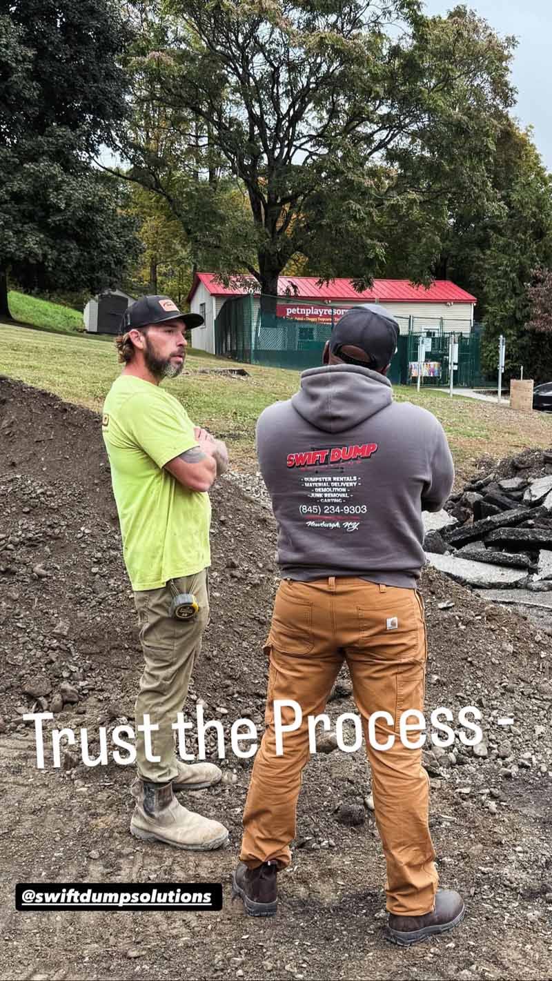 Two people in work clothes stand outdoors near a fire pit under the text “Trust the Process.”