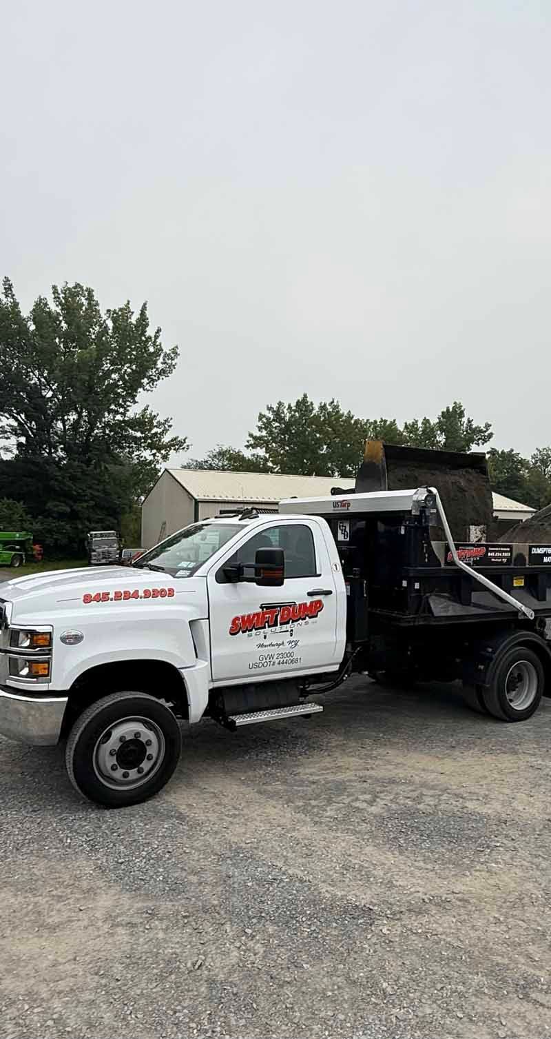 White tow truck parked on gravel, with black flatbed raised and trees in the background.