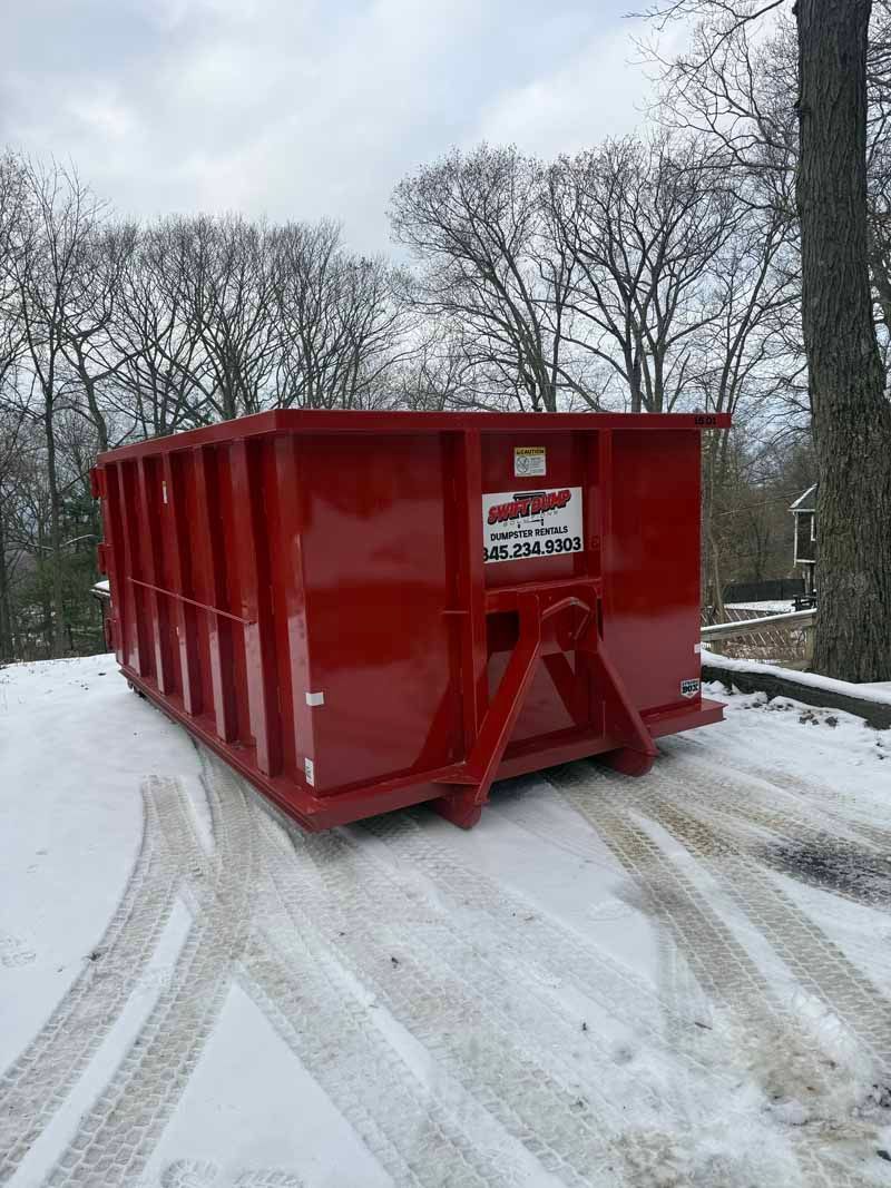 Red dumpster on a snowy road beside bare trees
