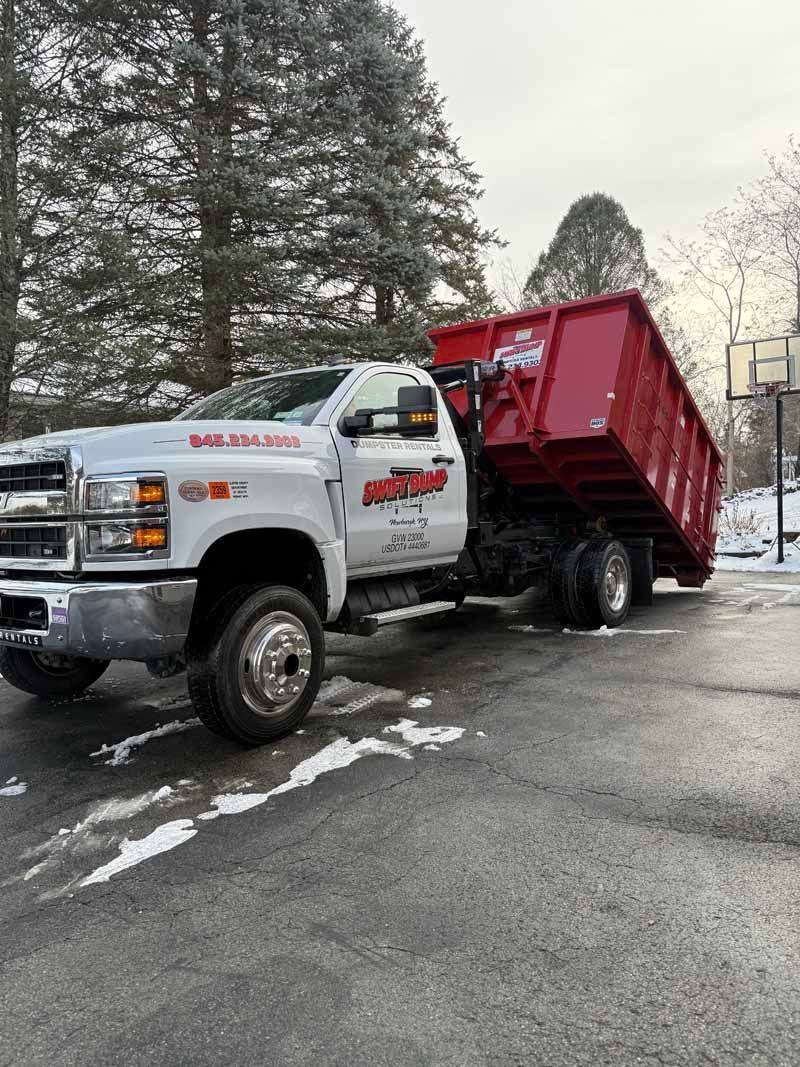 White dump truck tipping a red dumpster in a snowy parking lot