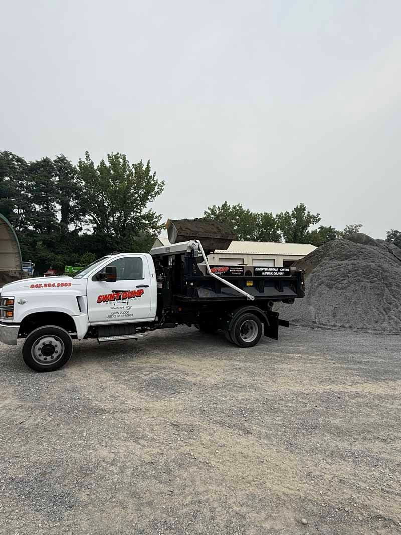 White-and-black dump truck parked on gravel beside a large pile of rocks in an industrial lot