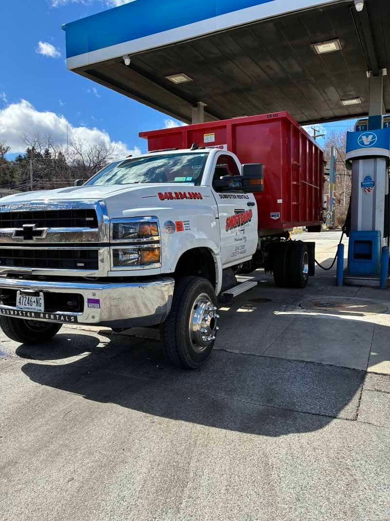 White dump truck with a red cargo bed at a gas station under a blue canopy.