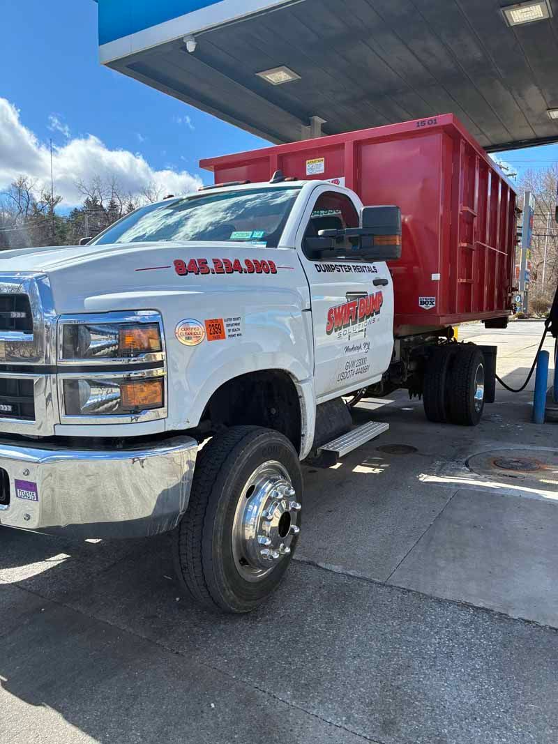 White dump truck with red cargo bed parked at a gas station under a canopy.