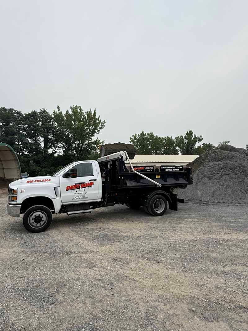 White dump truck parked on gravel beside a large pile of rocks under an overcast sky