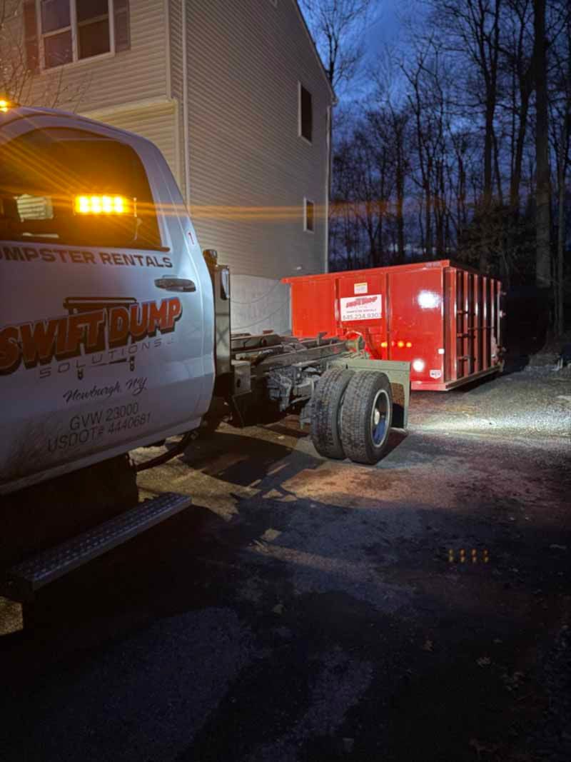 Truck cab hooked to a red trailer outside a building at dusk, with trees in the background.