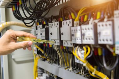 Hand holding a screwdriver inside an electrical control panel with wires and circuit breakers