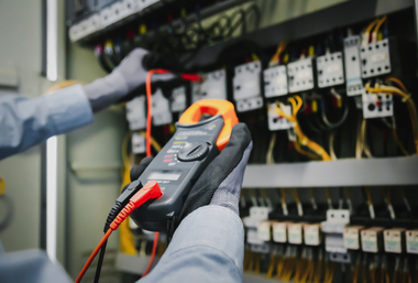 Gloved technician testing an electrical control panel with a digital multimeter.
