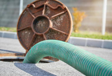 Green corrugated hose over a manhole opening beside a rusty metal cover outdoors