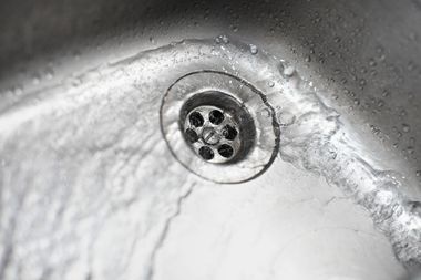 Close-up of a metal sink drain with water spots and limescale buildup