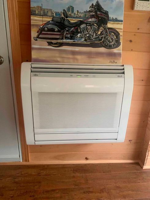 Un climatiseur blanc mural, installé sur un mur lambrissé sous une reproduction de moto.