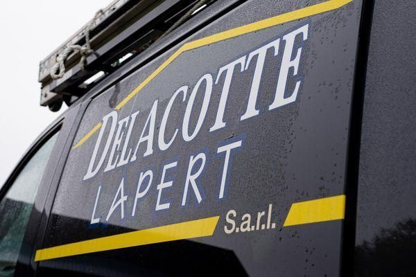 Fourgonnette noire avec le logo « DELACOTTE LAPERT Sarl » en blanc et jaune.