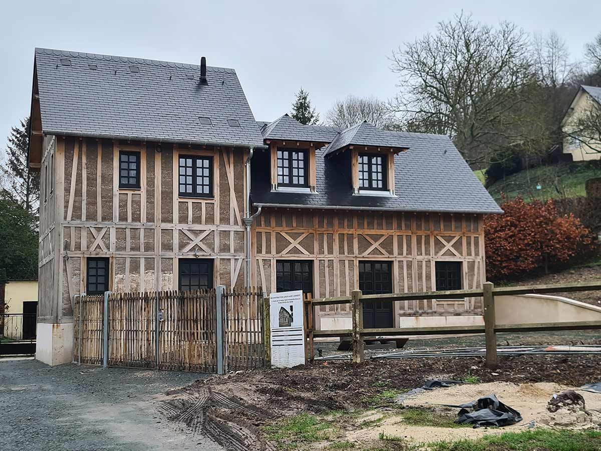 Une maison traditionnelle à colombages avec un toit en ardoise, des encadrements de fenêtres sombres et une clôture en bois