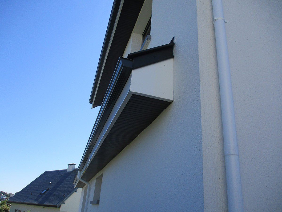Angle extérieur d'un bâtiment avec un toit sombre et un soffite clair s'étendant depuis le niveau supérieur.
