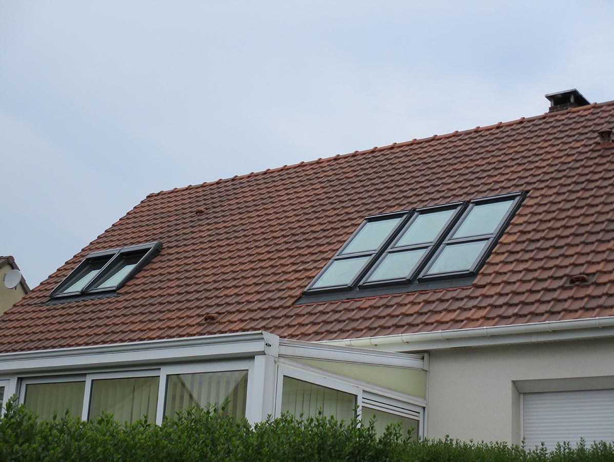 Un toit de tuiles percé de deux lucarnes surplombe une structure blanche avec une terrasse couverte