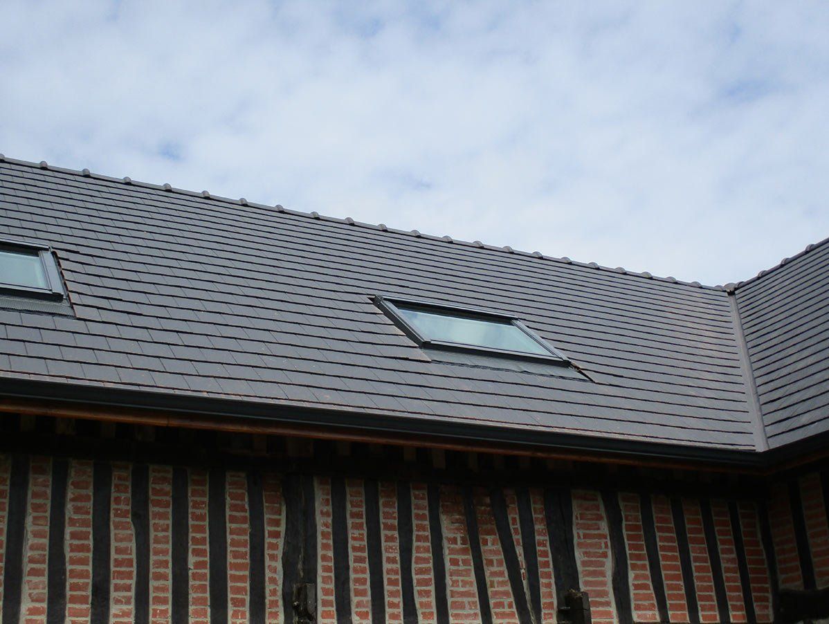 Un toit de tuiles ondulées percé de deux puits de lumière coiffe une maison traditionnelle à colombages