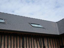 Un toit de tuiles ondulées percé de deux puits de lumière coiffe une maison traditionnelle à colombages