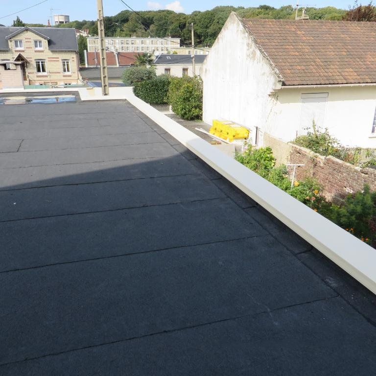 Toit plat noir avec bordures blanches et vue sur les bâtiments.
