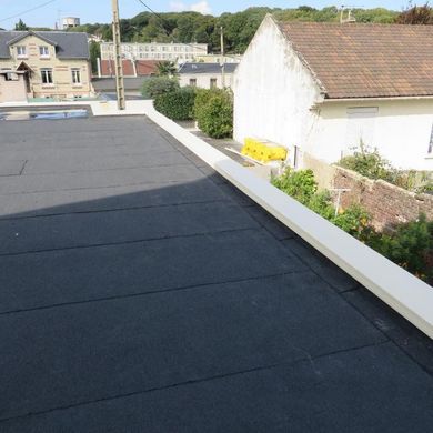 Toit plat noir avec des bordures blanches et des maisons à proximité.