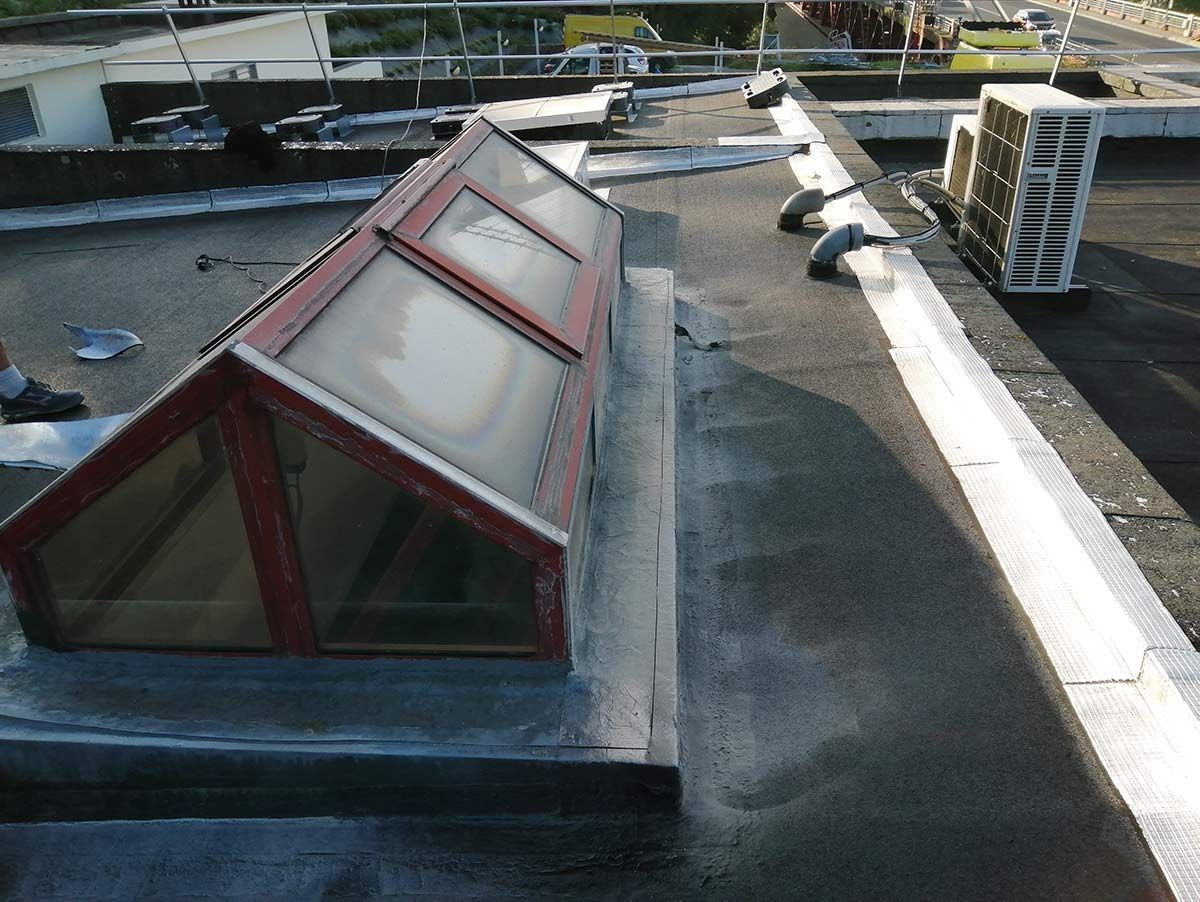 Puits de lumière sur un toit plat, entouré de matériaux de couverture et de quelques engins de chantier.